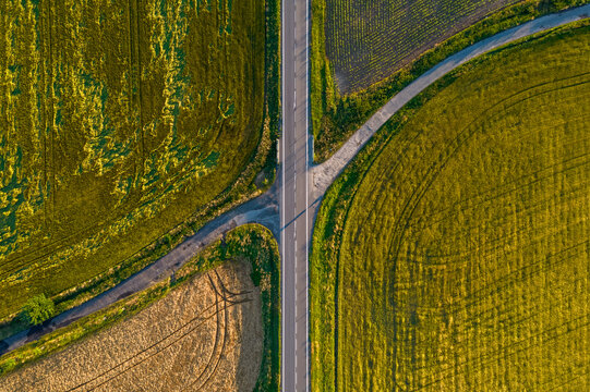 Aerial view of a road intersection surrounded by golden agricultural fields and green meadows in the Czech Republic.