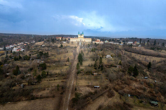 Aerial view of the Basilica of the Visitation of the Virgin Mary in Svaty Kopecek, surrounded by rolling hills, fields, and residential houses in Czech Republic.