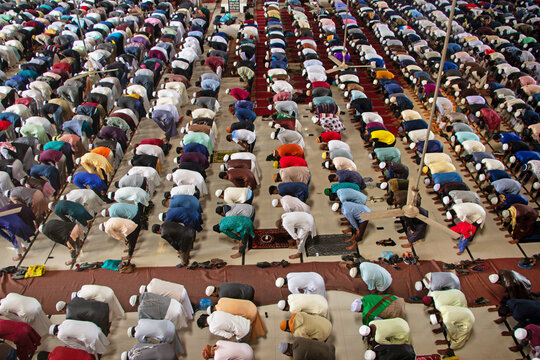 Dhaka, Bangladesh - 24 December 2021: Aerial view of Baitul Mukarram National Mosque showing a large congregation of men in traditional clothing performing prayer in orderly rows on the tiled floor.