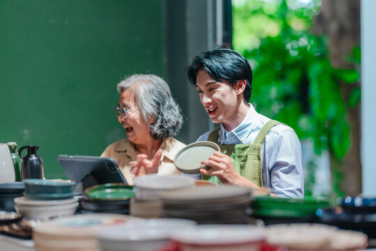 Mother and son small business owners filming live stream with smartphone in ceramic warehouse