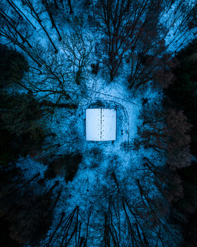 Aerial view of a small building surrounded by a dense forest covered in snow during winter in Czech Republic.