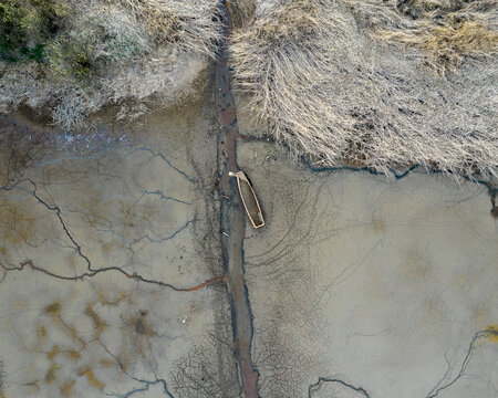 Aerial view of a small boat resting in a narrow channel within a vast expanse of cracked, dry mud and withered vegetation in the Czech Republic.