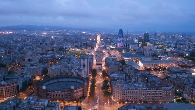 Aerial drone cinematic cityscape of Barcelona at twilight over Plaza de Toros Monumental with illuminated streets and urban architecture.