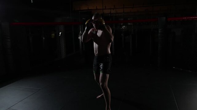 Male fighter training and boxing in dark combat arena, athletic workout footage.