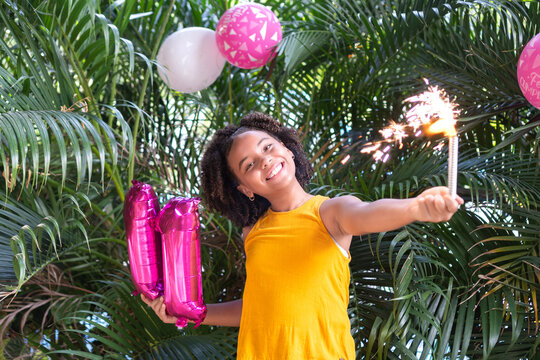 Girl celebrating 11th birthday holding sparkler and balloons