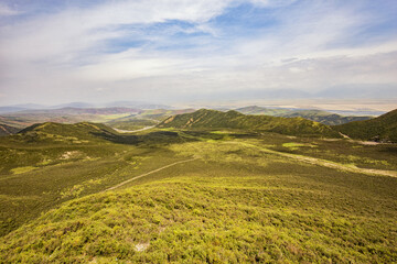 Fototapeta premium A wide panoramic view of rolling green hills and valleys under a partly cloudy blue sky, showing natural grassland terrain.
