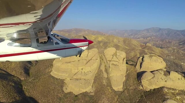 Closeup profile view of a small Cessna airplane flying by a formation of sandstone knobs near Vasquez Rocks in the San Gabriel Mountains of Southern California.