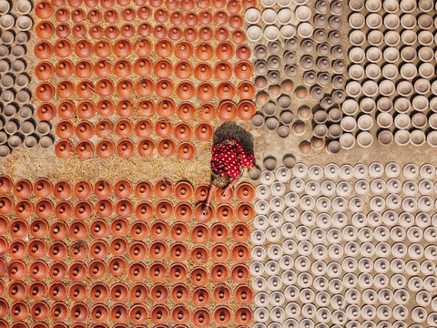 Brahmanbaria, Bangladesh - 03 November 2021: Aerial view of a person in a red patterned dress arranging numerous clay pots in organized rows on the ground during the pottery making process.
