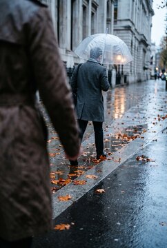 A man walking down a wet city sidewalk holding a clear umbrella during an autumn rain shower