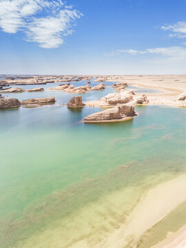 Unique water-covered yadan landforms stand in clear turquoise water under a bright blue sky, surrounded by arid desert terrain.