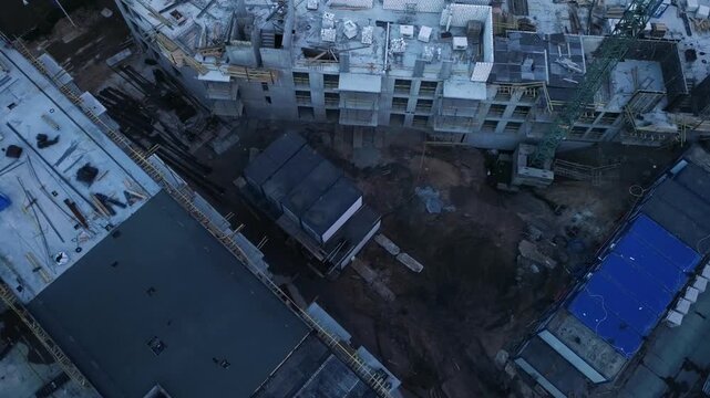 Aerial drone view of multi story apartment complex construction site with heavy machinery and green tower crane.