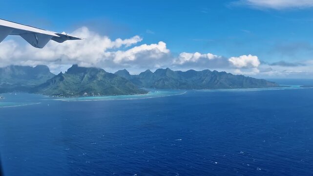 Aerial view from plane window over tropical island with lush green mountains and turquoise lagoon.