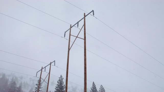 Wooden electrical transmission towers standing in snowy mountain landscape during winter storm.