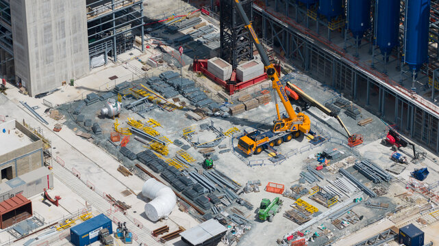 London, United Kingdom - 16 July 2026: Aerial view of a busy construction site featuring a large yellow mobile crane, stacks of steel beams, industrial pipes, and equipment.