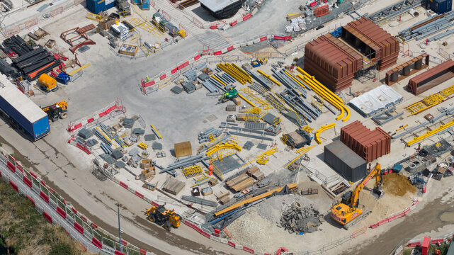 London, United Kingdom - 16 July 2026: Aerial view of a busy construction site featuring heavy machinery, yellow steel beams, storage containers, and piles of gravel.