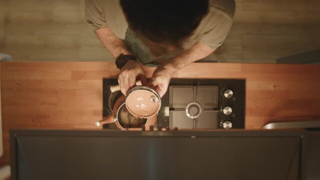 Man lifting lid off copper teapot to check tea brewing on stove, top down view