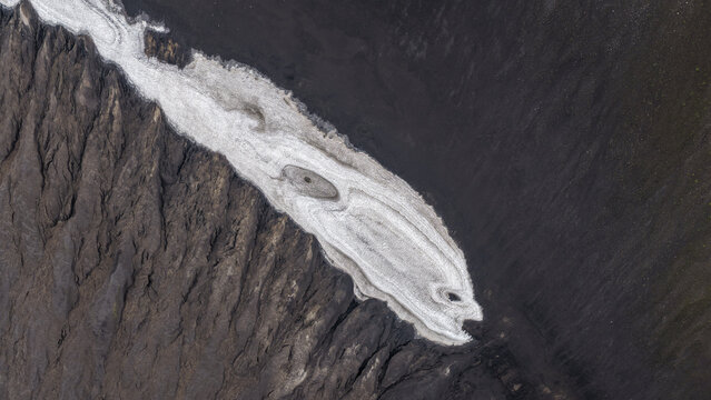 Aerial view of Landmannalaugar showing a glacier tongue contrasting with dark volcanic terrain in Hella, Rangarthing ytra, Iceland.