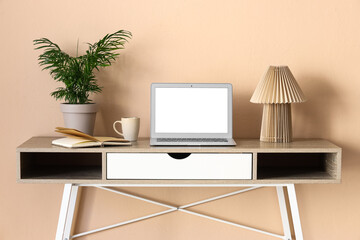 Fototapeta premium Remote work and home office setup, laptop with blank screen on a modern desk with plant and lamp against a peach wall