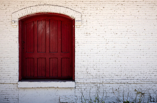 Vintage red wooden arched window shutters set in a painted white brick building wall background with copy space.
