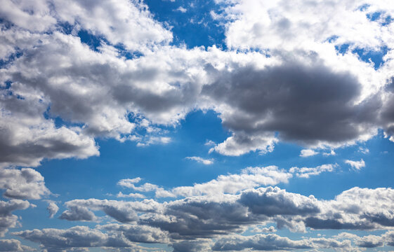 Dramatic sky background filled with fluffy white and grey cumulus clouds under bright sunlight
