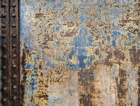 Heavily rusted industrial metal plate texture with blue paint remnants and rivets