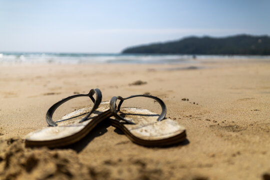 Flip flops on a sandy beach with ocean and tropical headland