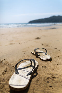 Flip flops on a sandy beach with ocean and tropical headland
