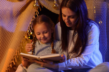 Fototapeta premium Family bonding and childhood development, mother reading a book to her daughter in a cozy blanket fort at night