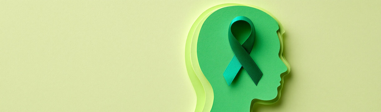 Mental Health Awareness: A teal ribbon symbolising mental health awareness is placed inside a green paper cut-out silhouette of a human head, representing the mind and psychological well-being.