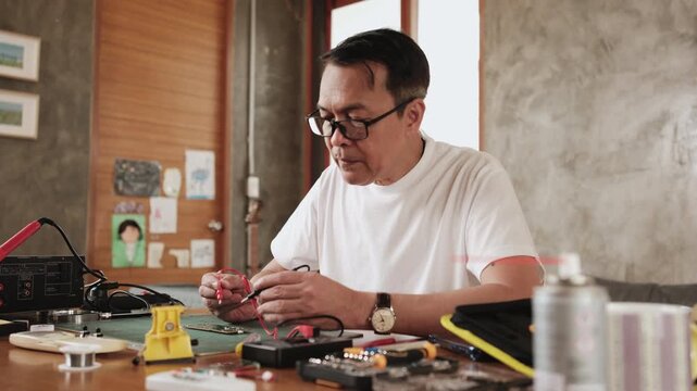 Mature Asian man checking soldering circuit board job with multimeter, cheers with job achievement, home electronics appliance repair successful, DIY fix tools, electrical component workshop hobby.
