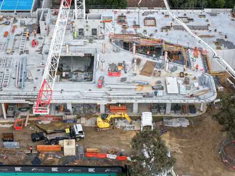 Melbourne, VIC, Australia - 24 August 2026: Aerial view of a construction site in Croydon featuring a tower crane, a yellow excavator, and workers on a concrete slab.