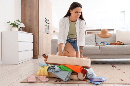 Travel packing stress and overpacking challenges, woman struggling to close an overflowing suitcase for vacation
