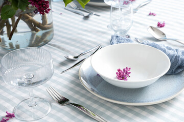 Fototapeta na wymiar Spring dining table setting with lilac flowers, elegant dinnerware, and striped tablecloth for special occasions