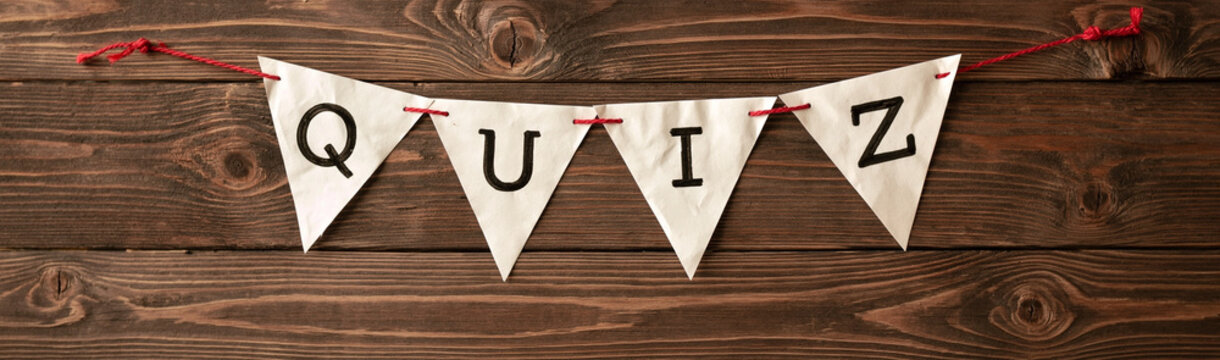Quiz Banner with Wooden Background: A charming triangular fabric banner with the word QUIZ written in bold black letters, strung across a rustic wooden plank background.