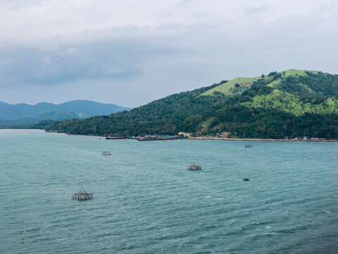 Ajuy, Philippines - 23 August 2026: Aerial view of the coastal landscape in Ajuy, featuring lush green hills, turquoise waters, and traditional fishing structures in the bay under a cloudy sky.