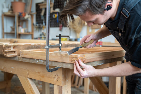 Crafter restorer checking smoothness of corners with patches on antique window frame at worktable, focused craftsman working on renovation of vintage wooden furniture in private woodworking studio.