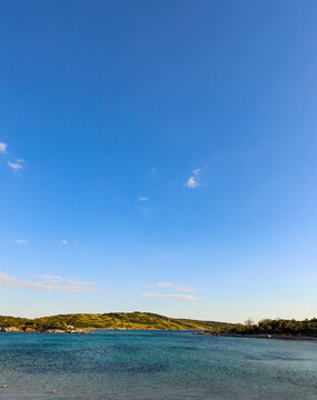 Coastal landscape showing calm turquoise water and green hills under a clear blue summer sky, suggesting tranquility and vacation