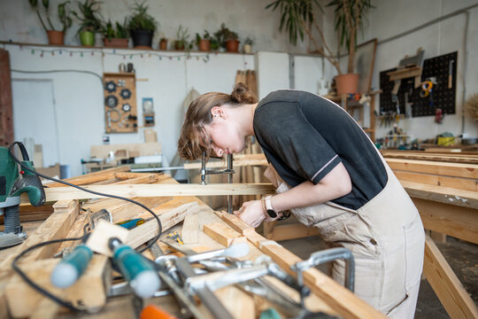 Concentrated woman restorer remodeling and remaking old wooden details for window frame in workshop, professional female carpenter at workbench in woodworking studio, handmade craft and skills.