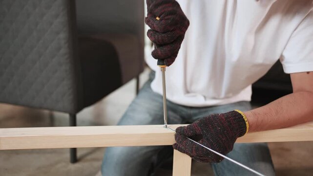 Close-up, man's hand screwing, self-assembling wooden furniture with DIY tools, tightening strength with a screwdriver, home improvement, hobby carpentry workshop, expert handyman, active lifestyle.