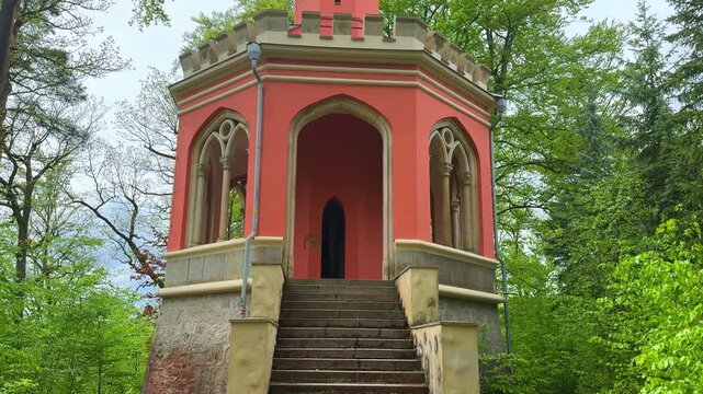 A small building stands with a staircase in Karlovy Vary, Czechia. Trees surround the structure, and the sky is partially cloudy. The area looks quiet and inviting. Tower - View of Charles IV