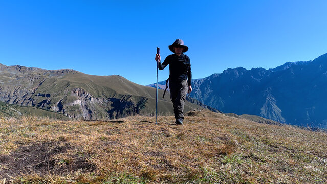 Hiker walking on a mountain ridge under a clear blue sky, exploring rugged wilderness.