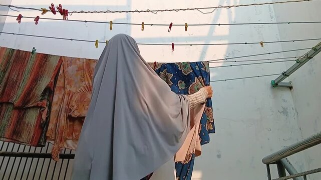 Woman Taking Dry Clothes Off a Clothesline After Air Drying Outdoors