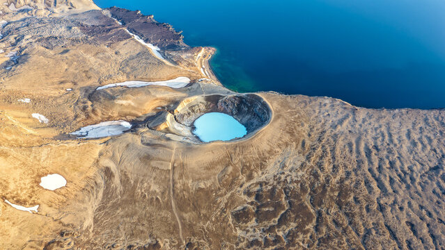 Aerial view of the Viti crater at Askja caldera with its vibrant blue geothermal lake, surrounded by rugged volcanic terrain and snow patches in Husavik, Nordurthing, Iceland.