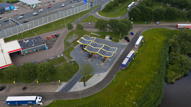 Amsterdam, Netherlands - 09 June 2026: Aerial view of a modern electric vehicle charging station featuring solar panel canopies, situated near a highway and a canal.