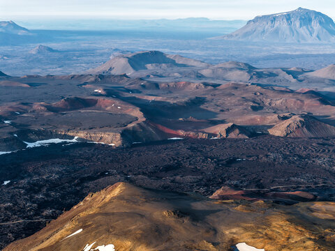 Aerial view of the volcanic landscape of Askja caldera with rugged lava fields, craters, and patches of snow under a clear sky in Husavik, Nordurthing, Iceland.
