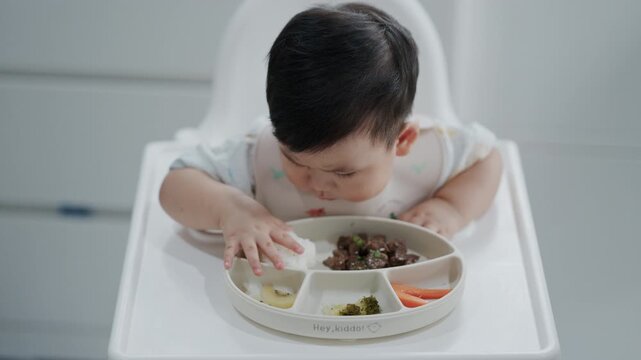 Asian baby boy self feeding sweet corn using baby led weaning method at home.	