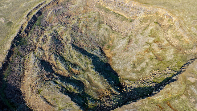 Aerial view of Litla-Viti volcanic crater with rugged rocky slopes, sparse green vegetation, and deep shadows in Husavik, Nordurthing, Iceland.