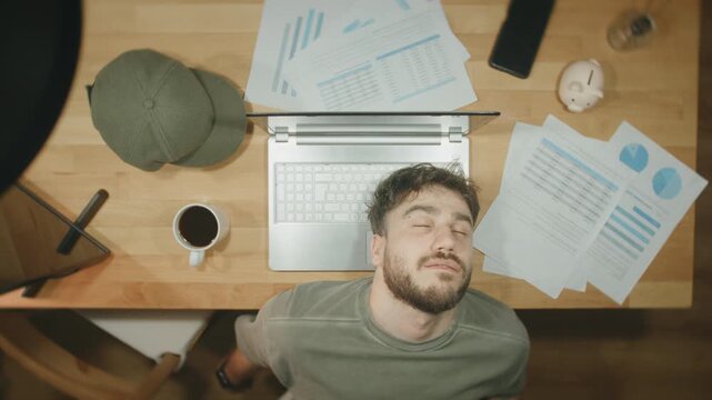 Tired man falling asleep at desk while working on finance reports, top view