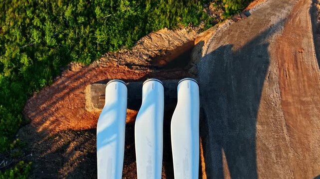 Wind turbine blades and tower sections on a construction site awaiting assembly in top down view