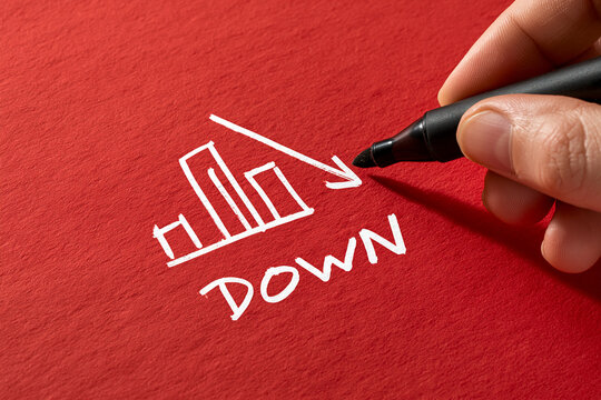 Hand drawing a downward bar chart with a black marker on red paper. A conceptual image for financial decline or economic recession analysis.